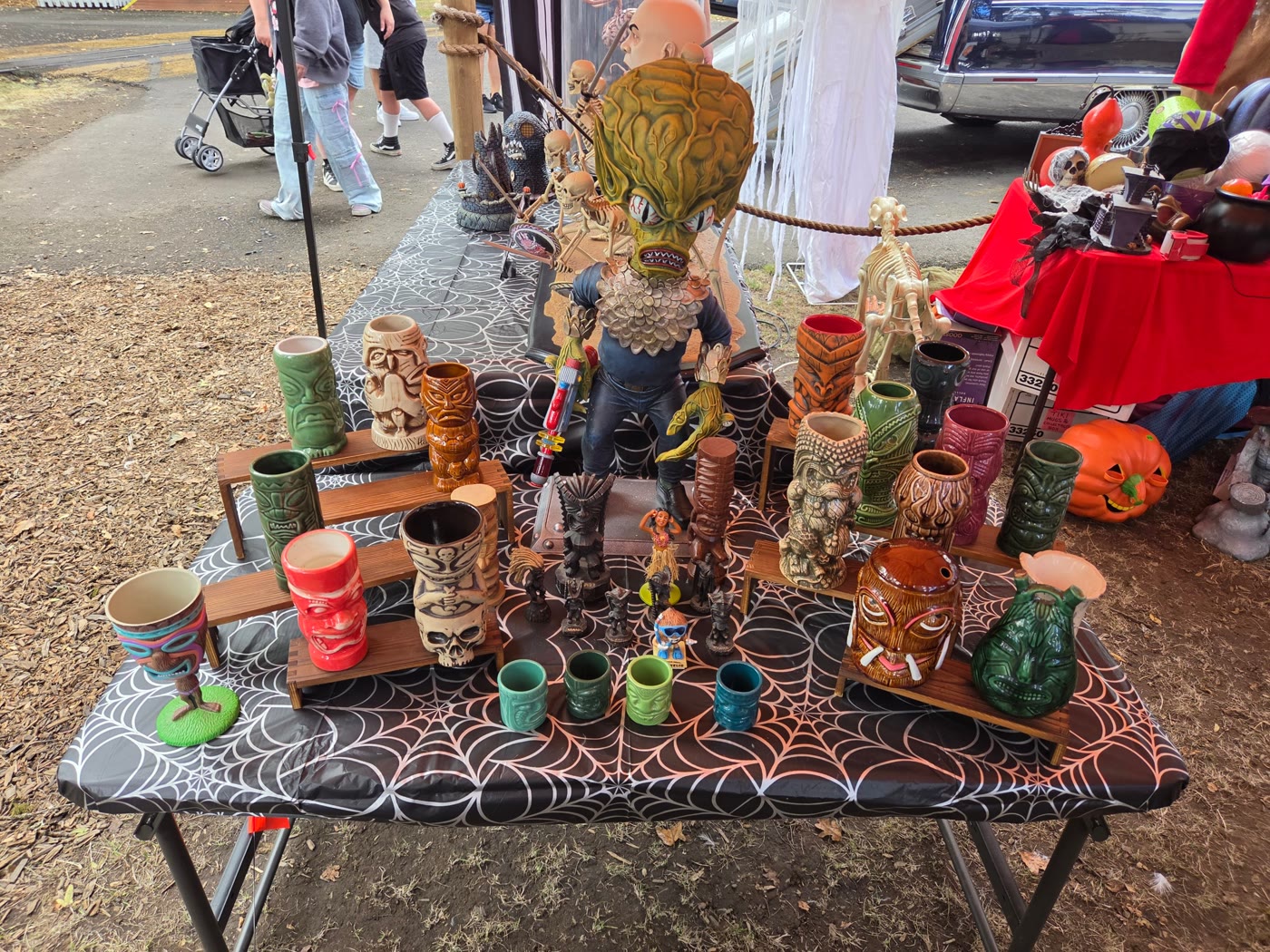 Table of vintage tiki mugs and a big-brained alien figure